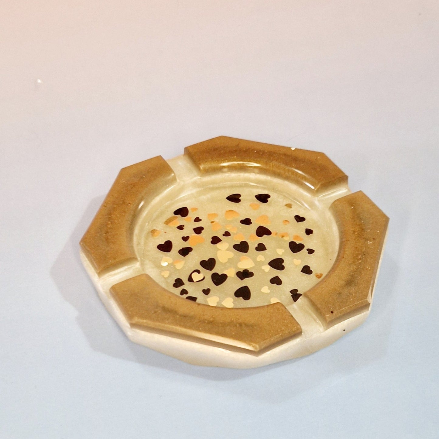 Cinzeiro decorativo em resina caramelo com efeito cobre, formato redondo com apoios e detalhe de corações no interior