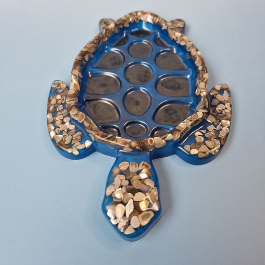Tartaruga decorativa artesanal em resina epóxi azul com detalhes de conchas, vista frontal sobre fundo claro.