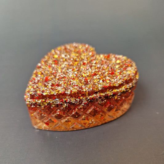 Caixa coração artesanal em resina epóxi, vista lateral, com efeito texturizado e mistura de glitter vermelho e dourado.
