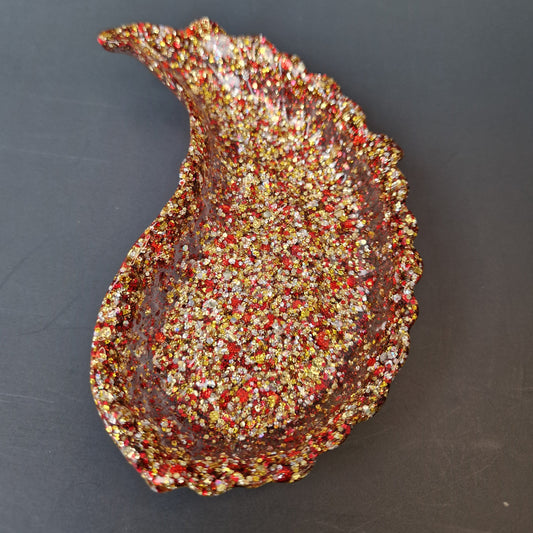 Asa decorativa em resina epóxi vermelho e dourado com glitter e bordas orgânicas, vista superior destacando a textura artesanal.