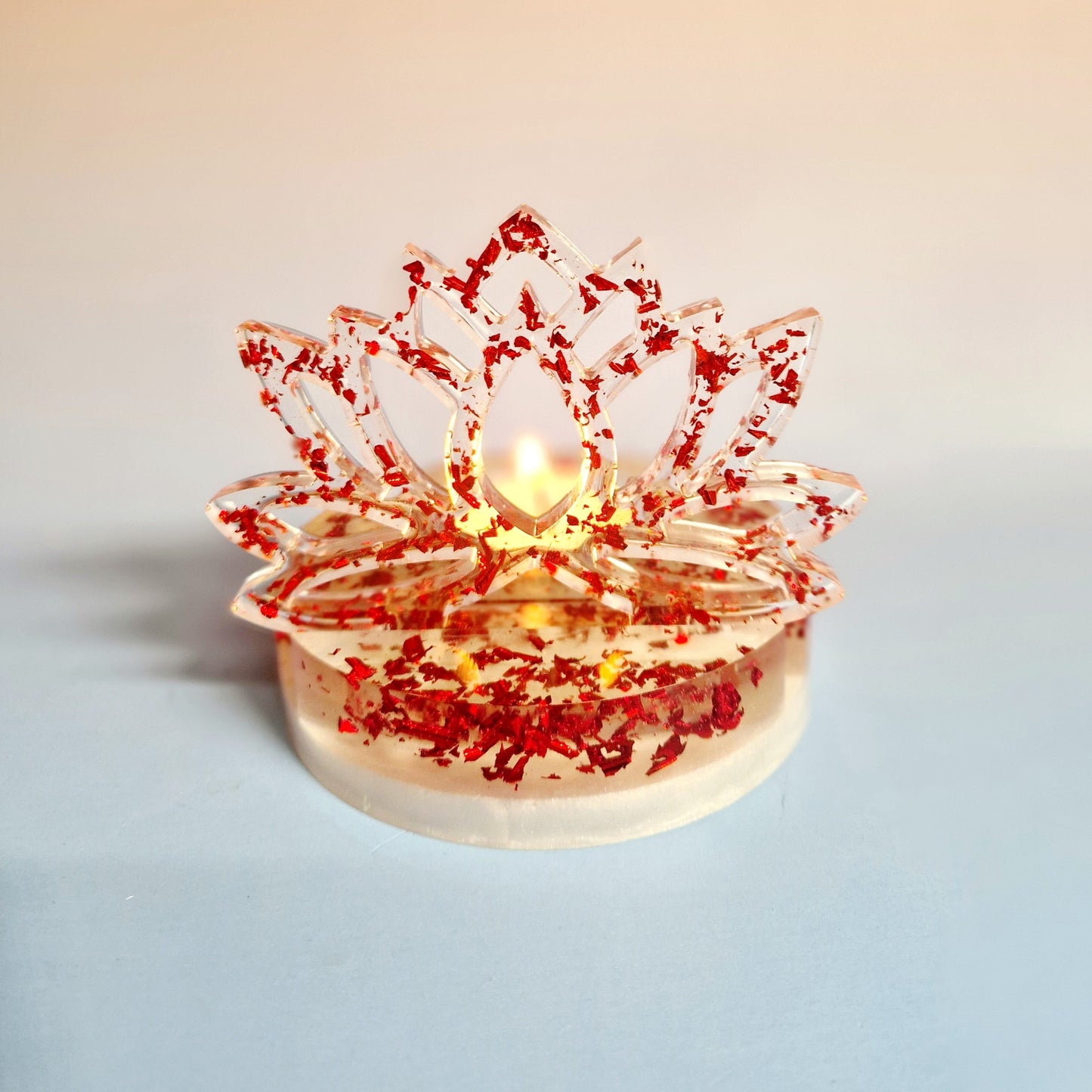Suporte de vela tealight em resina de alta transparência com a silhueta vertical de uma Flor de Lótus. A base e a flor são preenchidas com flocos metálicos vermelhos vibrantes, com uma vela de cera inserida no encaixe central