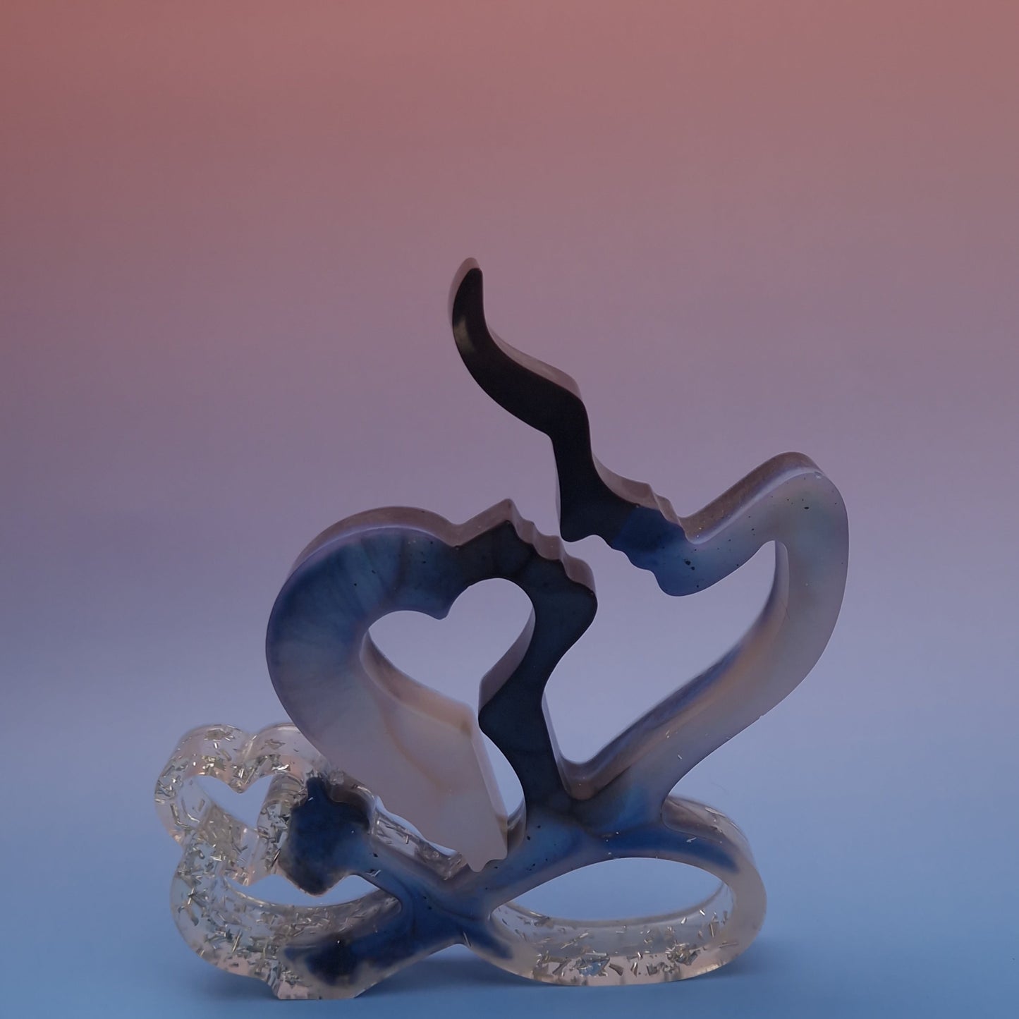 Escultura decorativa em resina epóxi representando um casal com coração vazado, em tons de azul, bege e transparente, acabamento artístico contemporâneo, vista frontal.