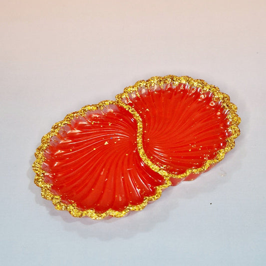 Taça decorativa Twin Shells em resina vermelha, com formato de conchas duplas, acabamento brilhante e bordas com efeito dourado texturizado, vista superior.