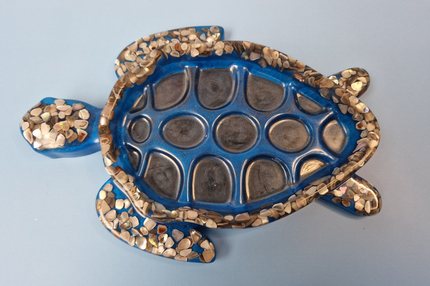 Tartaruga decorativa azul em resina epóxi com conchas naturais incrustadas, vista superior da carapaça texturizada.