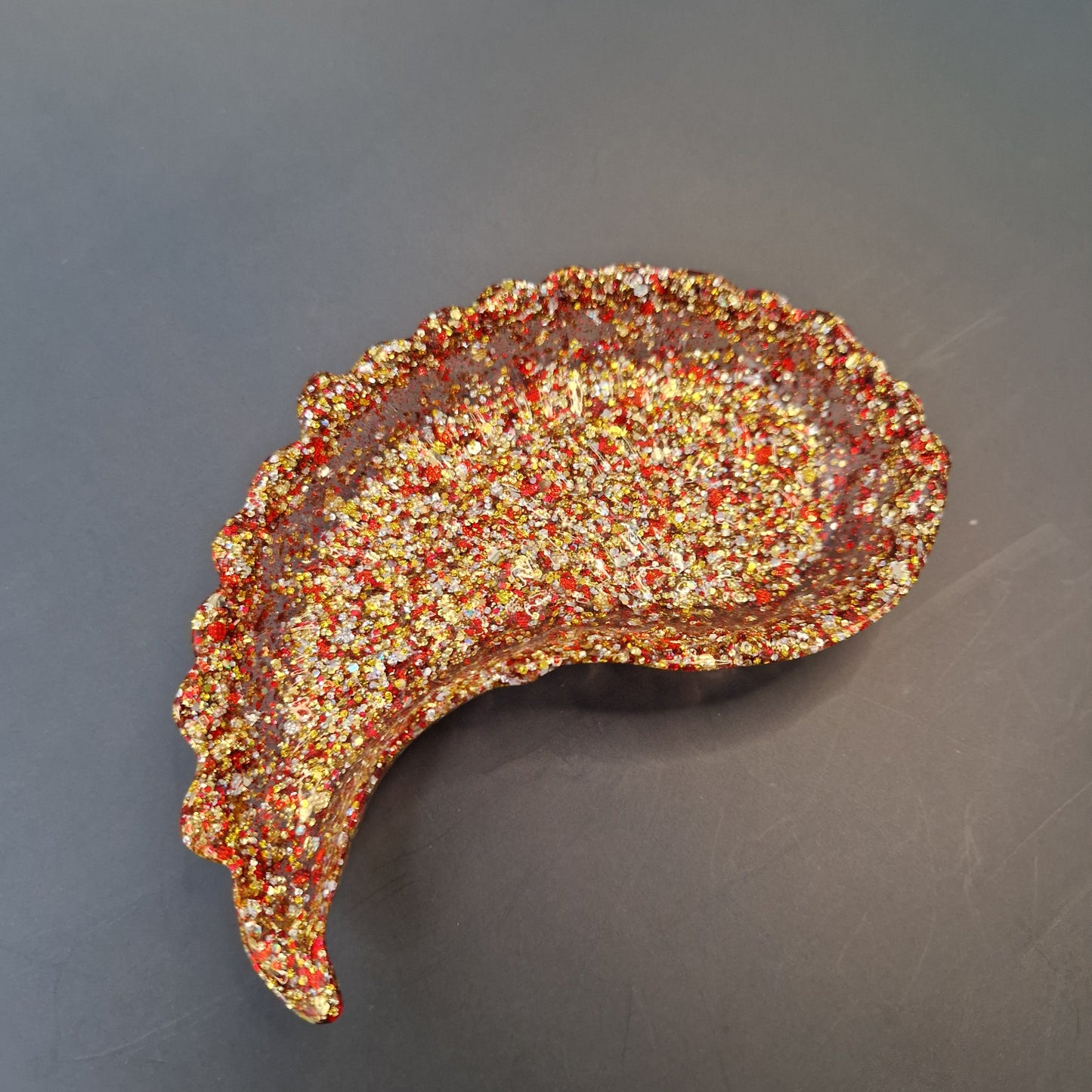 Asa decorativa em resina epóxi nas cores vermelho e dourado, com acabamento texturizado e brilho, vista lateral sobre fundo escuro.
