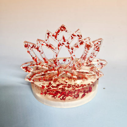 Suporte de vela em resina transparente com silhueta de Flor de Lótus e flocos metálicos vermelhos em fundo neutro.