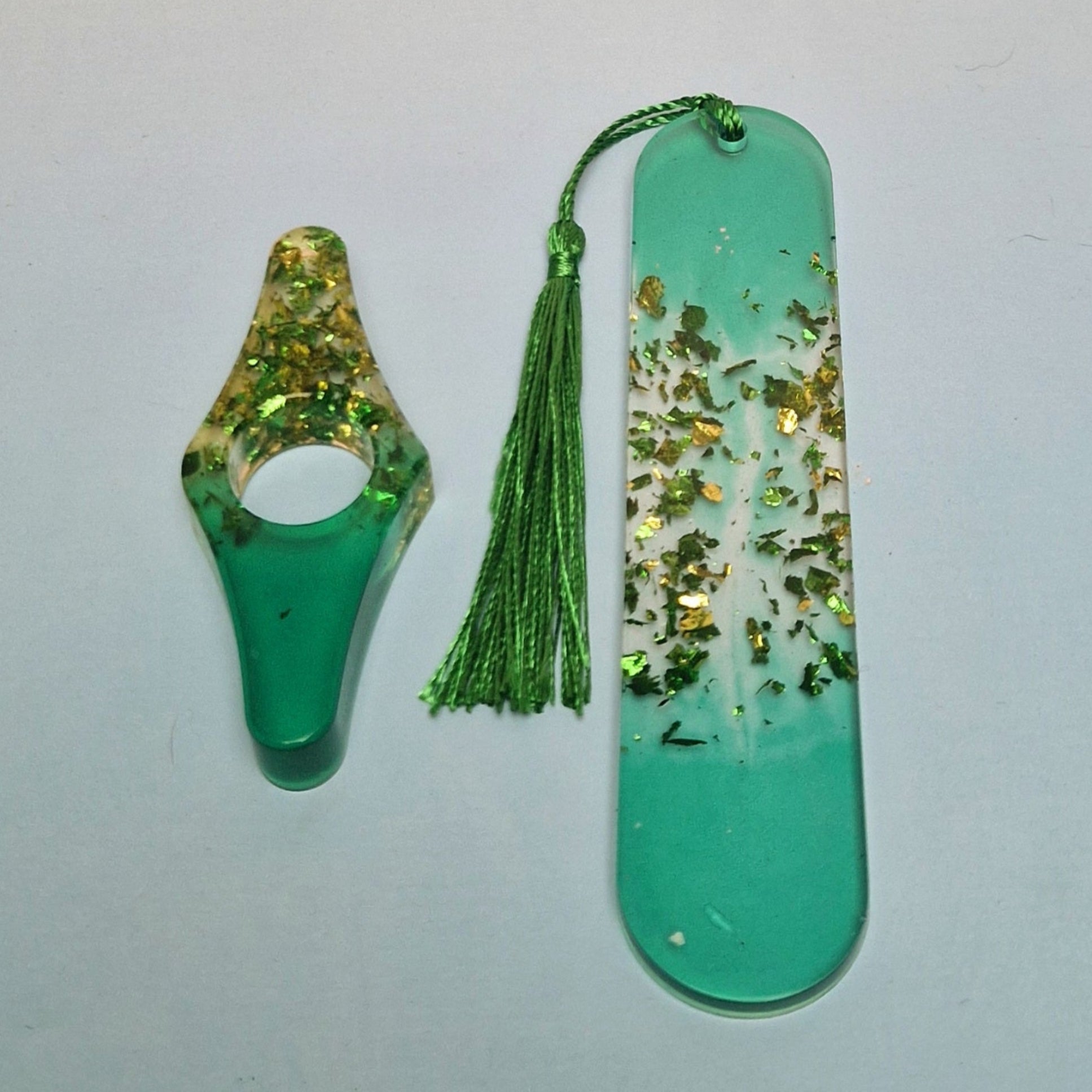 Conjunto artesanal em resina verde com marcador de página retangular, detalhes dourados e pingente de tassel verde, acompanhado de acessório decorativo curvo.