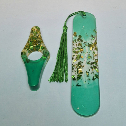 Conjunto artesanal em resina verde com marcador de página retangular, detalhes dourados e pingente de tassel verde, acompanhado de acessório decorativo curvo.