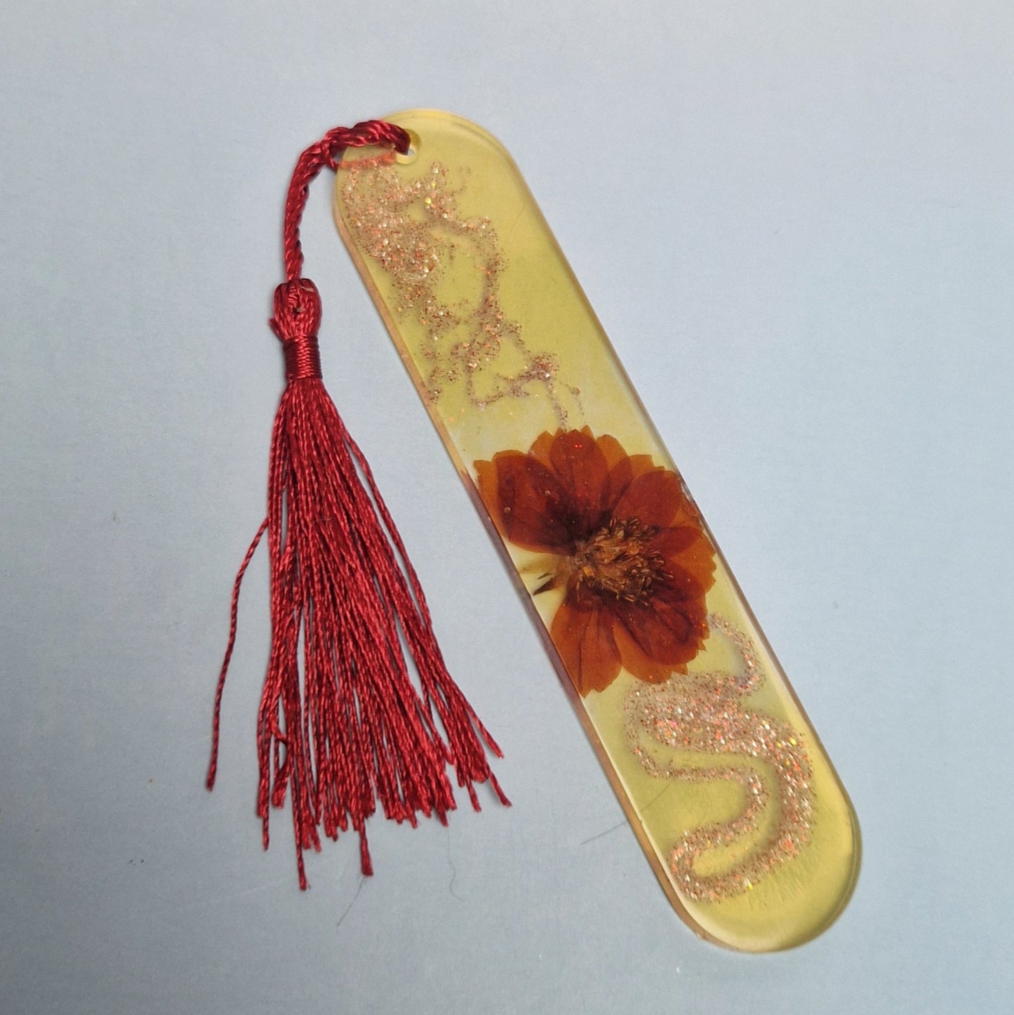Marca-páginas artesanal em resina epóxi amarelo com flor natural encapsulada, detalhes brilhantes e tassel vermelho