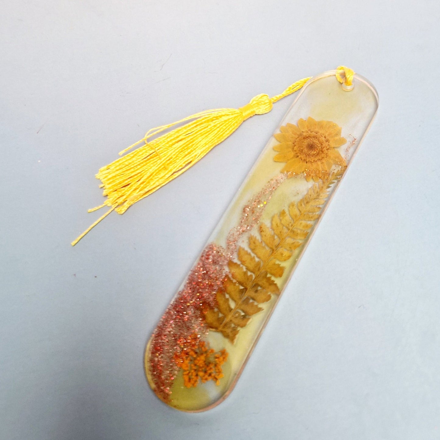 Marca-páginas artesanal em resina epóxi com flores e folhas naturais secas, acabamento translúcido e tassel amarelo