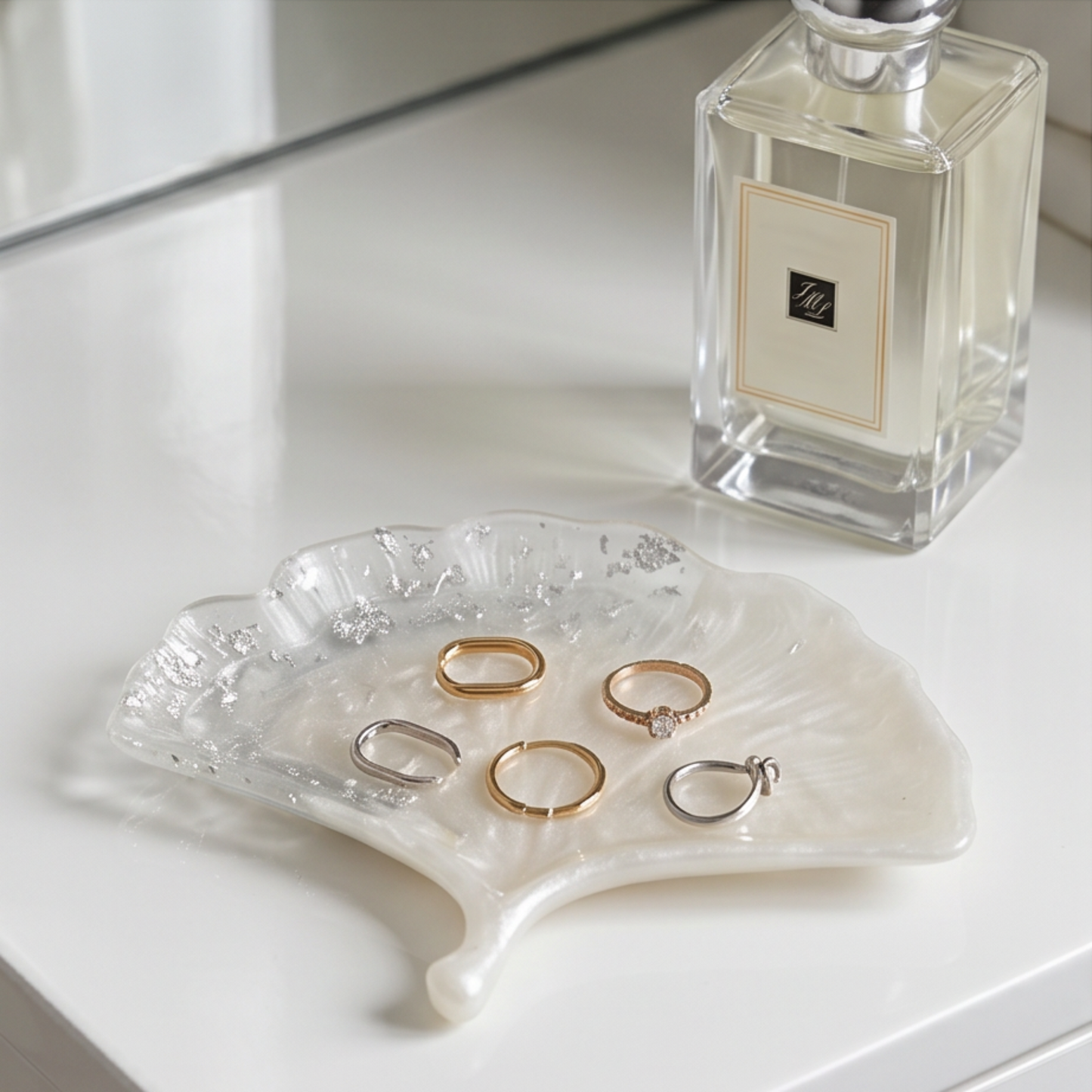 Prato decorativo Ginkgo branco perlado com folha de prata sobre mesa de cabeceira, utilizado como organizador de anéis e joias.