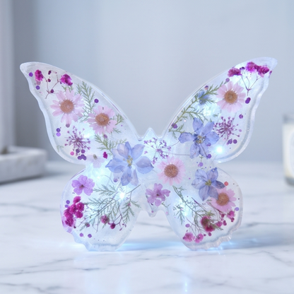 Borboleta Alice iluminada por luz LED, com flores naturais preservadas em tons suaves e acabamento translúcido iridescente.