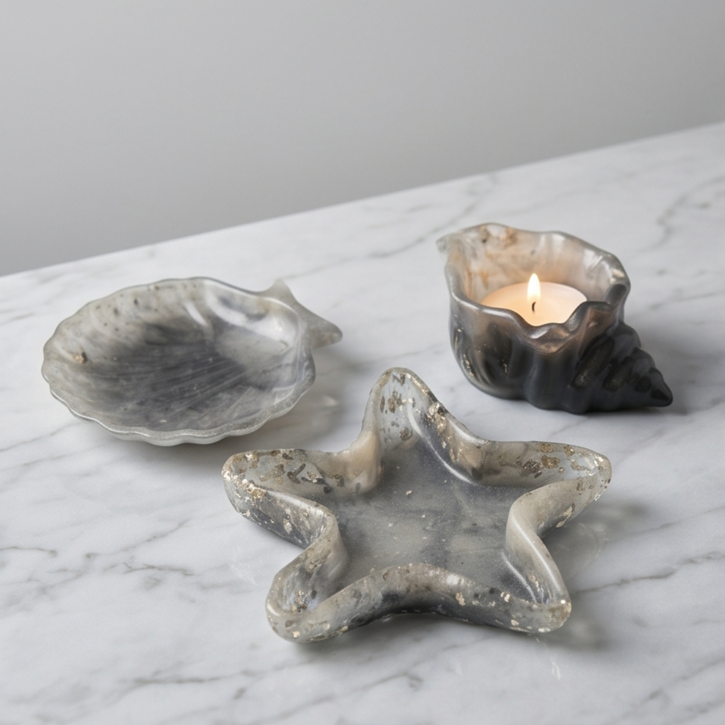 Conjunto decorativo em resina cinza com estrela-do-mar, concha e búzio sobre superfície de mármore